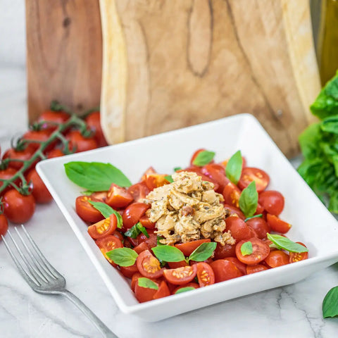 Loma Linda Pesto & Sun-Dried Tomato TUNO served with cherry tomatoes and fresh basil on a plate, vegan tuna alternative.