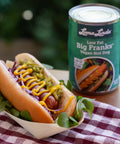 Single Loma Linda Big Frank on a bun with mustard, relish, and onions, served in a hot dog tray over a bed of arugula – plant-based hot dog alternative with classic toppings