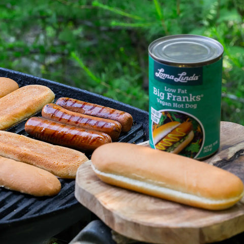 Three Low Fat Big Franks grilling alongside buns on an outdoor barbecue – plant-based hot dog alternative prepared for a classic cookout