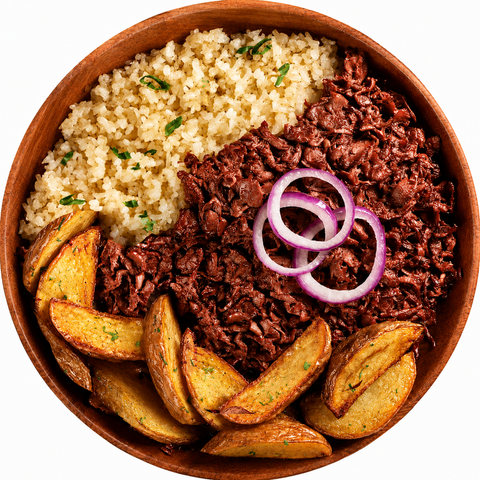Overhead view of a wooden bowl filled with a meal consisting of couscous, UnMeat corned beef style, potato wedges, and red onion rings on a white background.