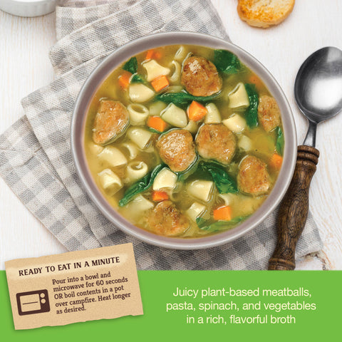 Bowl of Italian wedding style soup with plant-based meatballs, pasta, spinach, and vegetables on a checkered cloth.
