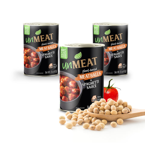Three cans of 'UmMeat' plant-based meatballs in spaghetti sauce with a wooden spoonful of beans and a tomato on a white background.